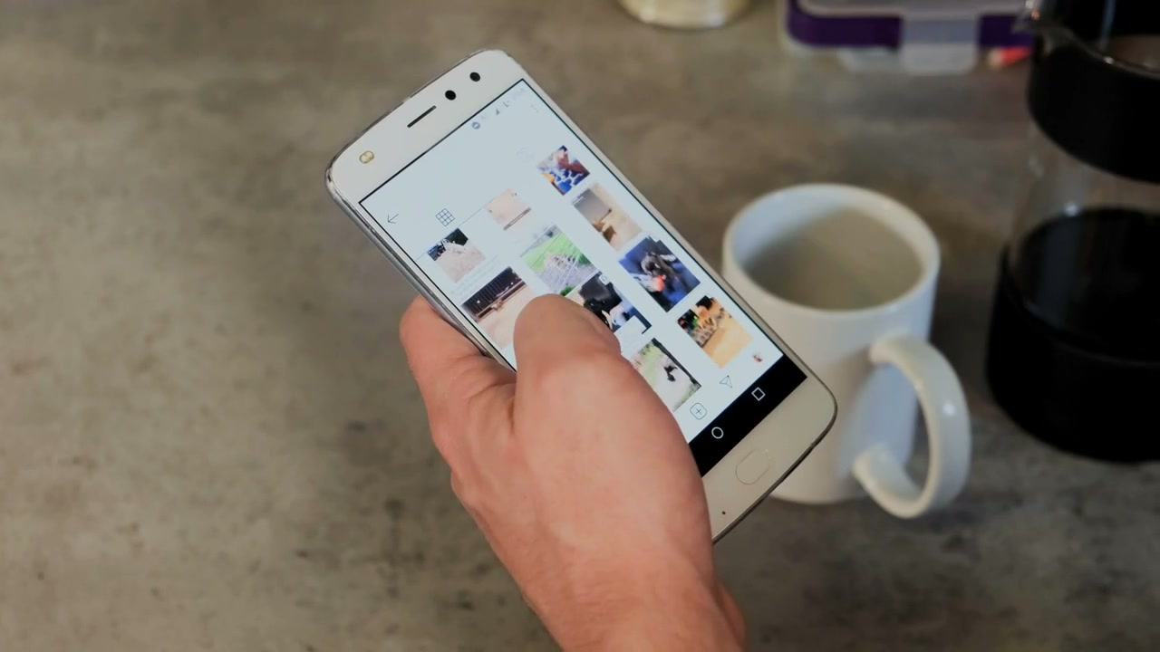 A person checks their phone while pouring coffee.